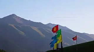 National flag of Kyrgyzstan with yellow, green and blue flags in front of a mountain at sunset