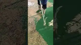 Worker spreads green liquid coating evenly across ground surface using roller