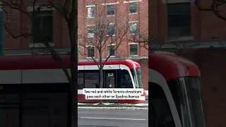 2 red-and-white Toronto streetcars pass each other on Spadina Avenue, under the watch of CN Tower