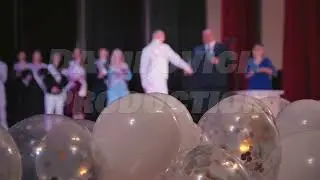 White balloons with confetti fill the foreground, celebrating a school graduation ceremony taking