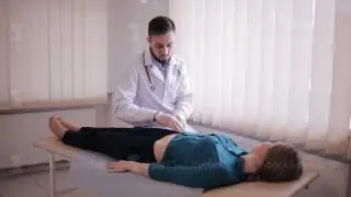 Male doctor makes palpation of the abdomen of the patient. The girl lies on a couch in the doctor's