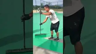 applying green acrylic coating to a sports court surface with a long squeegee for a smooth finish