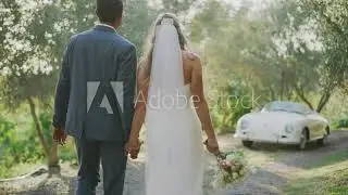 Multi ethnic couple walking holding hands together in the afternoon sun on their wedding day, going