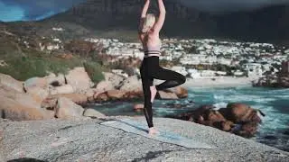 Woman Meditating In Yoga Warrior Pose At The Ocean, Beach  And Rock Mountains. Yoga Pose