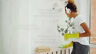 Cheerful maid African American girl is doing housework dusting using cloth and wearing gloves, young