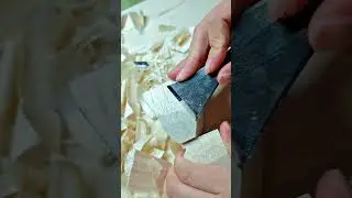 carving and slicing small pieces of white wood using a very sharp metal tool on the wooden surface