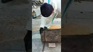 cutting a large brown tree trunk using a small electric chainsaw tool on a tiled outdoor floor area