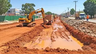 Red Soil Road Project Featuring Sequential Dump Trucks and Central Excavator