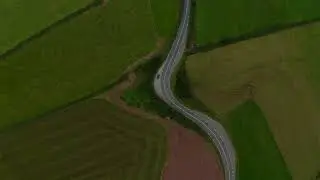 Aerial birds eye overhead top down view of series of curves on road surrounded by green fields
