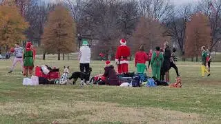 Students and dogs in Christmas clothing at a park playing kickball