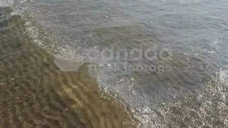 Slow motion sunlit lake wave stock video. Rippled sand pattern below. HD video.
