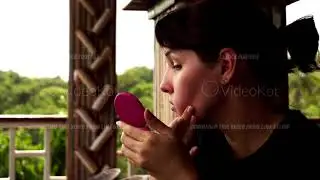 Closeup footage of young woman sitting in the open wooden balcony and looking at herself in mirror