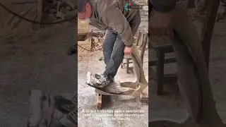 A skilled craftsman uses a specialized hand tool to shape wood, standing on the piece for stability.