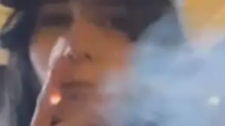 A brunette with long nails smokes a cigarette and litters