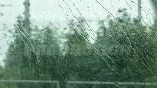 Rain droplets streaming down clear window glass on a wet, gray day