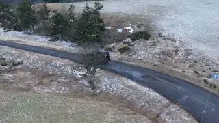 Black SUV driving on a curvy asphalt road from aerial perspective. Vehicle travels through snowy