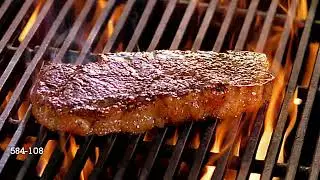 High angle close up steak being flipped over by spatula on flaming grill