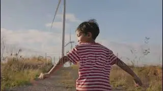 A Asian boy child run freedom in The windmill farm field producing clean energy. Concept of
