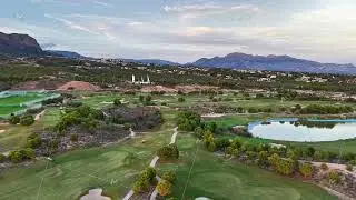 Stunning Aerial Perspective Showcasing Lush Golf Course With Mountain Background And Water Elements