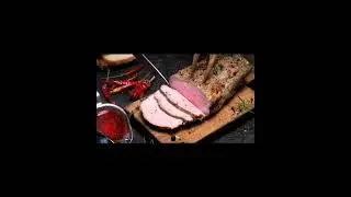 Human hand cutting baked tenderloin on wooden #cutting board surrounded with hot #cranberry s#auce