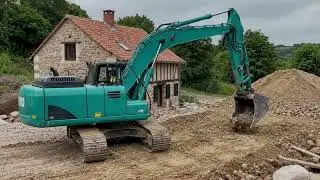 Green Excavator at Work Near Traditional Village Houses