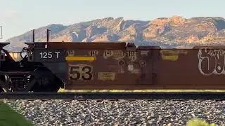Railroad train moving along pulling empty well railcars with some having graffiti on the sides