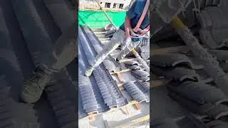 A construction worker carefully aligns roof tiles while ensuring precision and safety on the job