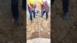 Two workers are using a gas-powered earth auger to drill a hole in the ground