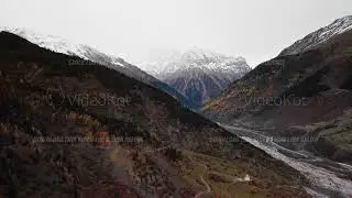 Expansive valley descent leading to snow clad summit amid rocky cliffs and dramatic sky