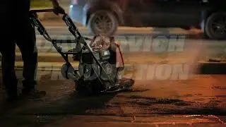 Worker compacting asphalt patching road at night during urban street repair