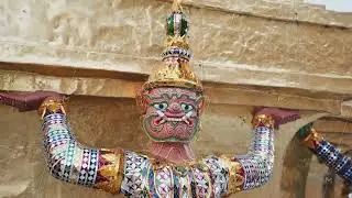 Close up of a colorful demonic Yaksha guardian statue holding up a golden stupa at Wat Phra Kaew