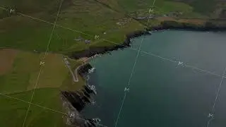 High angle footage of steep and high escarpments falling to water. Green pastures along rugged sea