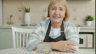 Portrait of beautiful elderly woman wearing apron sitting in kitchen alone and looking at camera