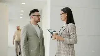 Girl and guy colleagues talking in office hall while people walking around