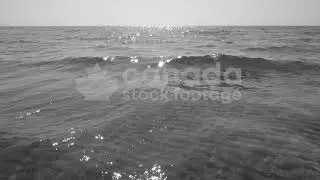 Slow motion sunlit crashing wave stock video. Rippled sand visible below. Black & white. HD video.