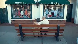 An Elderly Couple Sitting On A Sidewalk Bench