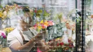 Handsome guy in apron changing open to close sign on flower shop window