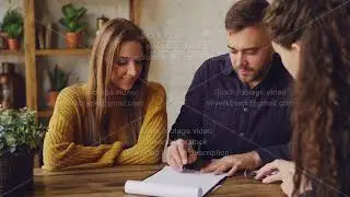 Female realtor is reading purchase and sell agreement to young couple, man is signing document and