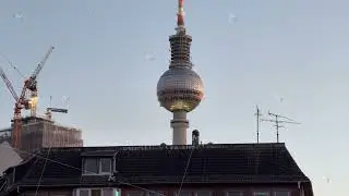 Handheld shot of Berlin TV Tower, Fernsehturm, rising above city buildings and cranes in