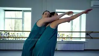 Two young adult Caucasian women in blue dresses are dancing modern ballet in studio