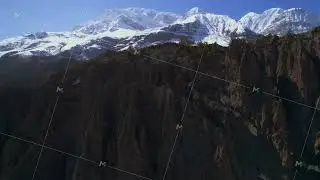 Aerial ascending rising view Himalaya mountains rocky formations with snowy peaks behind on sunny
