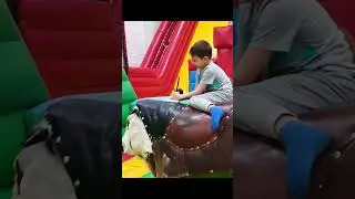 Kid tries to don't fall from the toy bull and play with boat