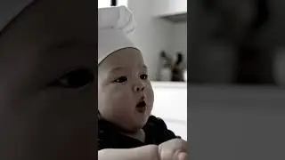 A baby, in tiny chef hat, critiques exotic fruit with serious expression.