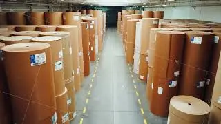 Huge warehouse of paper rolls for production of corrugated cardboard packaging. Drone shot, top view