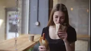 Beautiful girl eating a hot dog in a cafe.