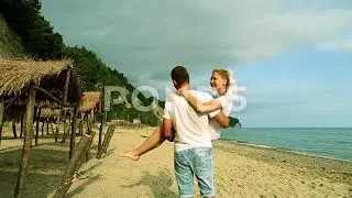 A man carrying a woman in his arms on the beach. Newlyweds at the sea.