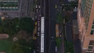 Aerial top down perspective of a BTS Skytrain moving through Bangkok, Thailand, at dusk alongside