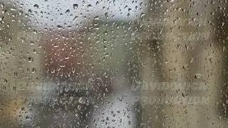 Raindrops flowing on window glass during rainy day blurring city buildings in background