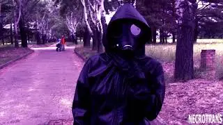 A girl in a black leather suit and an Israeli gas mask walks in a park near the river bank.