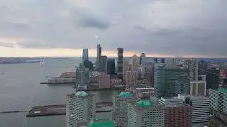 Jersey City skyline glimmering at sunset, clouds hovering over Hudson River, urban landscape in soft